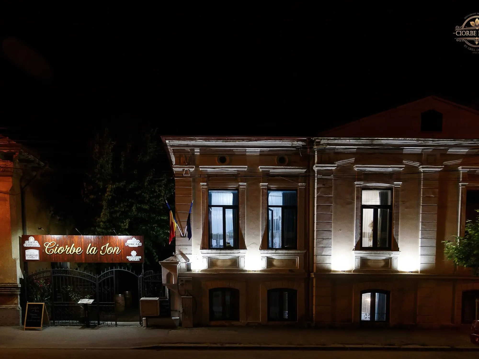 The restaurant building in the evening, the facade lit and the sign at the gate