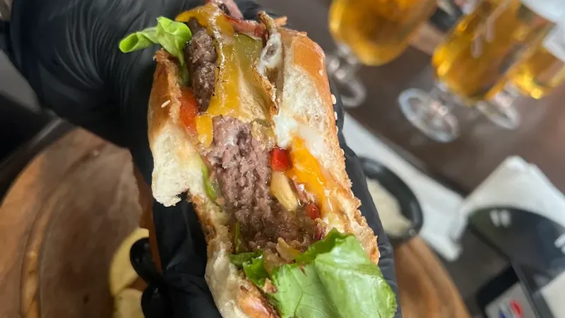 A burger cut in half, held above a wooden board, with glasses of beer behind