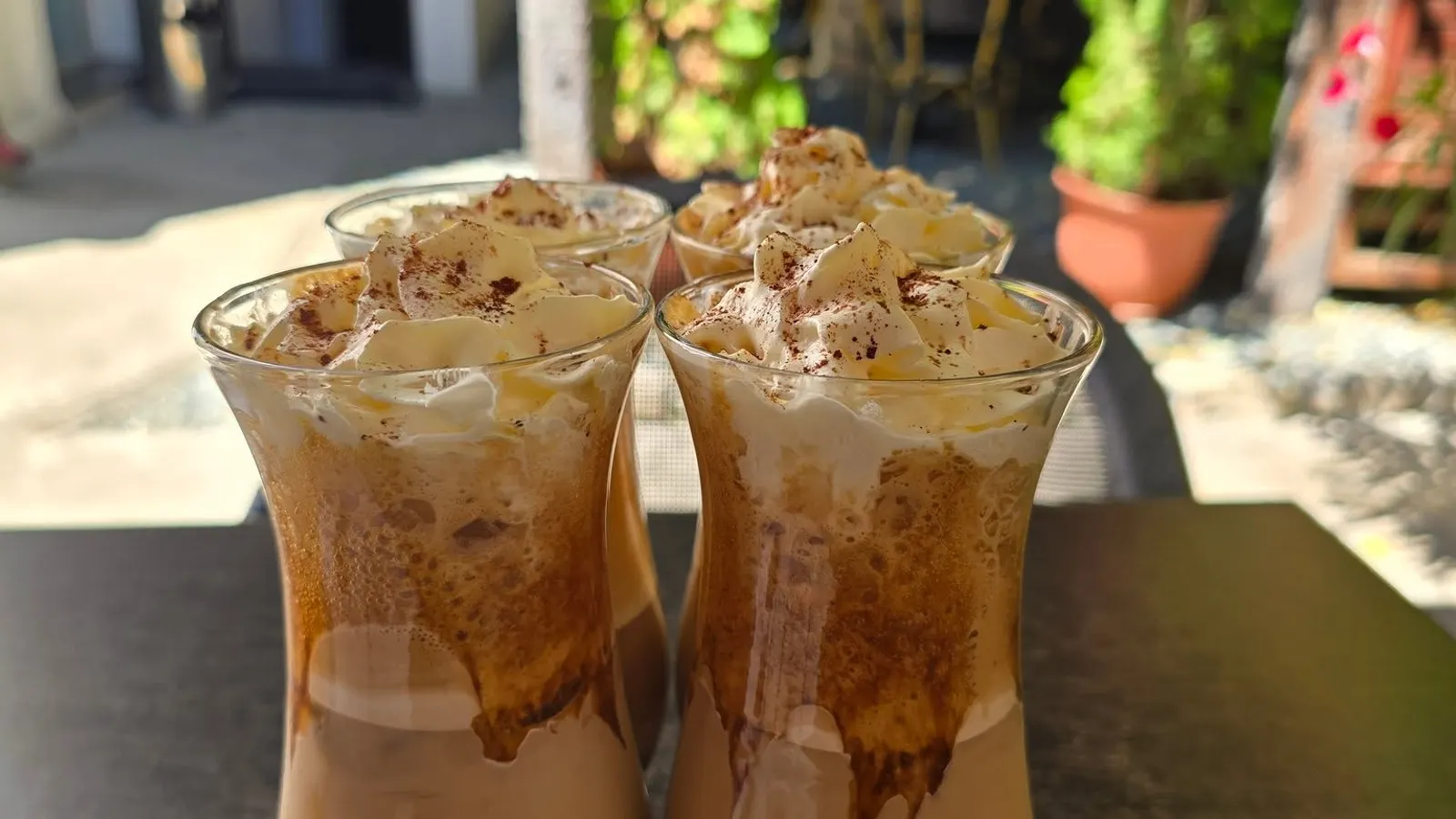Three glasses of coffee with whipped cream, on a table on the terrace
