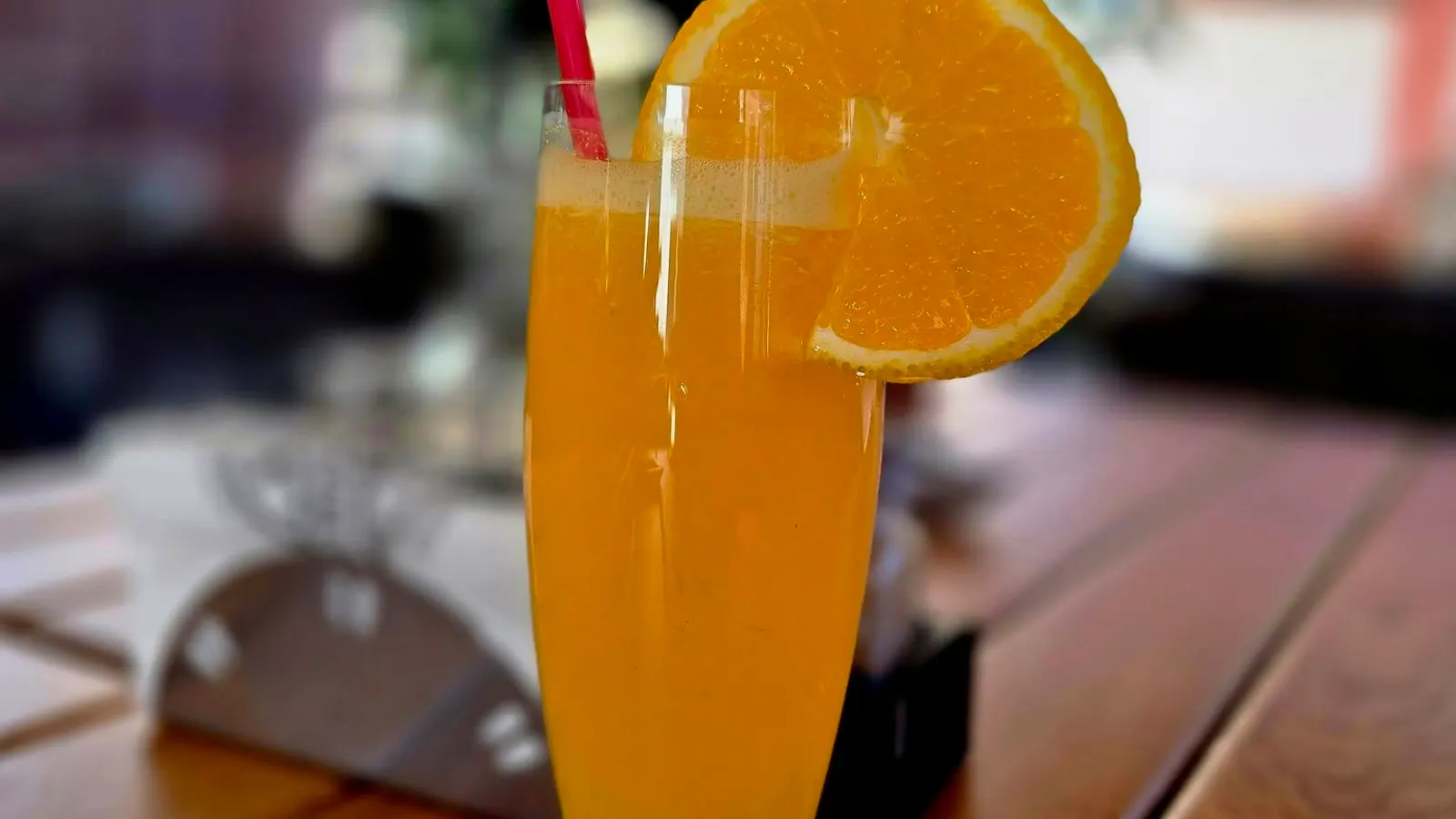 A glass of orange juice with a slice of orange on the rim, on a table on the terrace